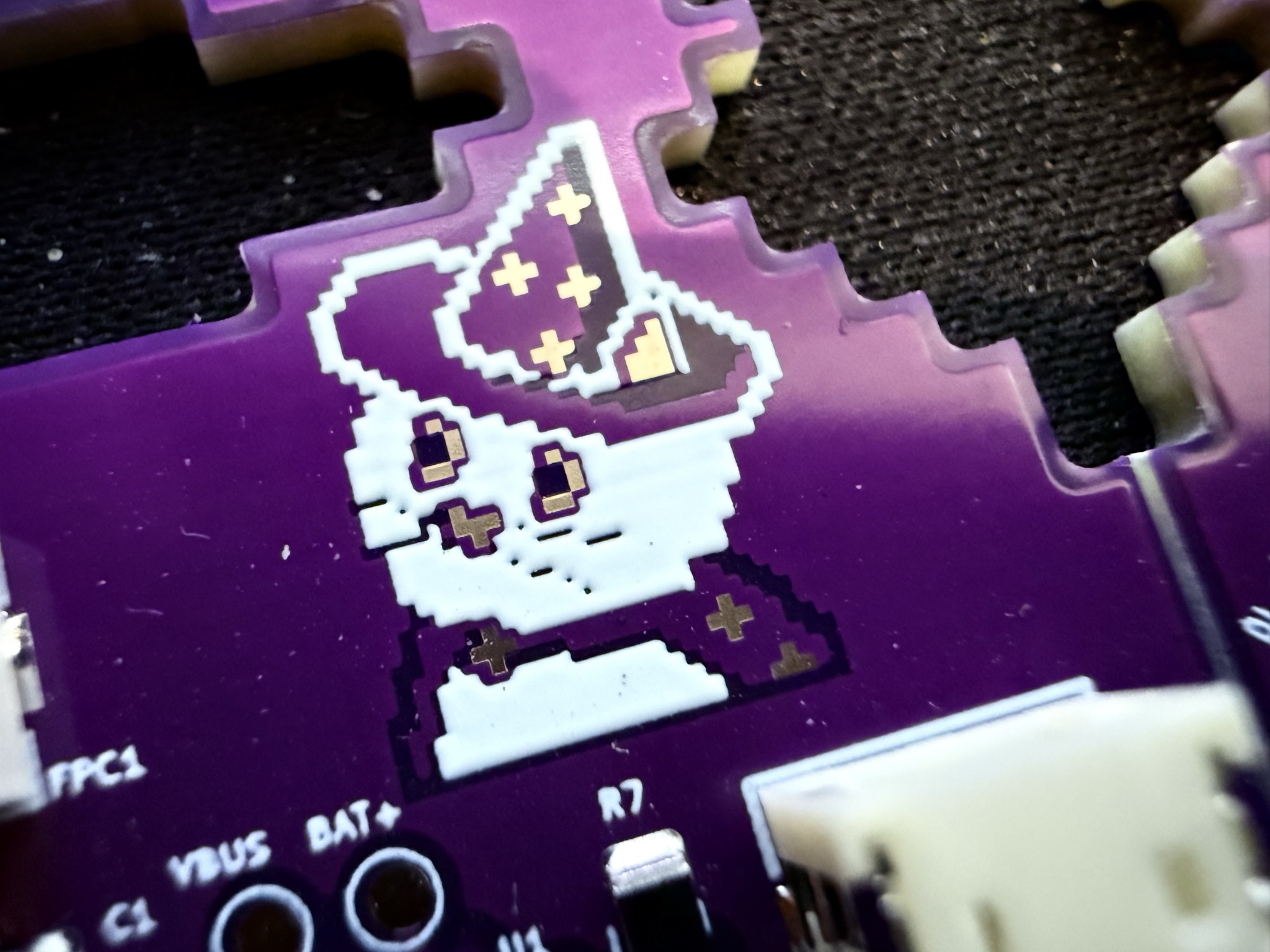 Retro pixel-art witch mascot silkscreen with golden stars on purple PCB